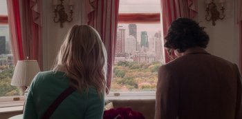 Movie still from “A Rainy Day in New York” (2019), directed by Woody Allen – Two women looking out of a window at a city skyline; Medium shot, Over the shoulder angle