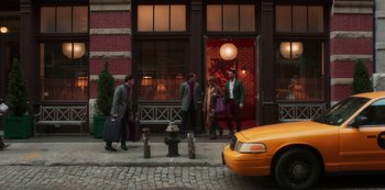 Movie still from “A Rainy Day in New York” (2019), directed by Woody Allen – A group of people standing on a sidewalk next to a fire hydrant; Wide shot, Over the shoulder angle