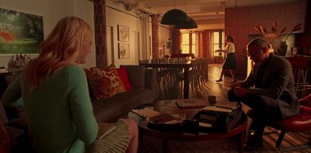 Movie still from “A Rainy Day in New York” (2019), directed by Woody Allen – A woman is sitting on a couch in a living room; Wide shot, Over the shoulder angle