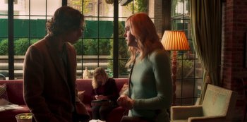 Movie still from “A Rainy Day in New York” (2019), directed by Woody Allen – A woman standing next to another woman on a pink couch; Medium shot, Over the shoulder angle