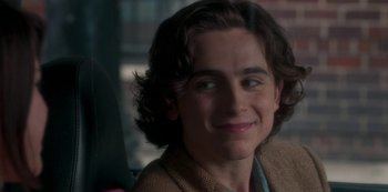 Movie still from “A Rainy Day in New York” (2019), directed by Woody Allen – A man with long hair is smiling for the camera; Close Up shot, Over the shoulder angle