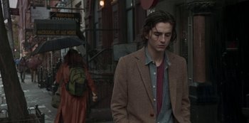 Movie still from “A Rainy Day in New York” (2019), directed by Woody Allen – A man in a brown jacket walking down a street; Medium shot, Low angle