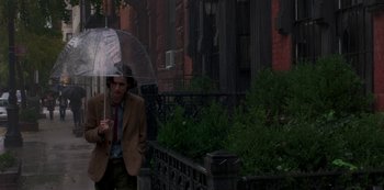 Movie still from “A Rainy Day in New York” (2019), directed by Woody Allen – A man holding an umbrella while standing on a sidewalk; Medium shot, Low angle