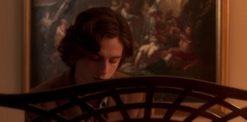 Movie still from “A Rainy Day in New York” (2019), directed by Woody Allen – A young man sitting in front of a painting; Medium shot, Over the shoulder angle