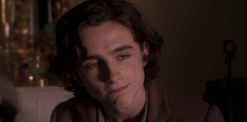 Movie still from “A Rainy Day in New York” (2019), directed by Woody Allen – A young man with long dark brown hair and wearing a brown jacket; Close Up shot, Over the shoulder angle