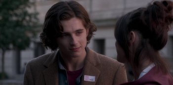 Movie still from “A Rainy Day in New York” (2019), directed by Woody Allen – A young man wearing a brown jacket and a red t - shirt; Close Up shot, Over the shoulder angle