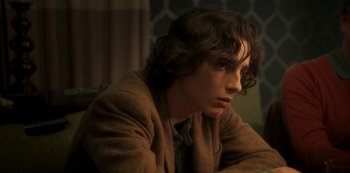 Movie still from “A Rainy Day in New York” (2019), directed by Woody Allen – A man with long brown hair sitting in a room; Close Up shot, Over the shoulder angle