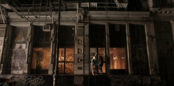Movie still from “A Rainy Day in New York” (2019), directed by Woody Allen – A man standing on a fire escape in front of a building at night; Extreme Wide shot, Low angle