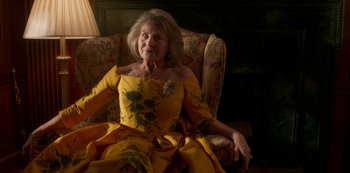 Movie still from “A Rainy Day in New York” (2019), directed by Woody Allen – An older woman in a yellow dress sitting in a chair; Medium shot, Low angle