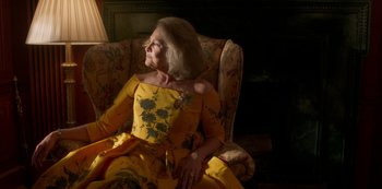 Movie still from “A Rainy Day in New York” (2019), directed by Woody Allen – An older woman wearing a yellow dress sitting in a chair; Medium shot, Low angle
