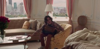 Movie still from “A Rainy Day in New York” (2019), directed by Woody Allen – A man sitting on a chair in a living room; Medium shot, Over the shoulder angle