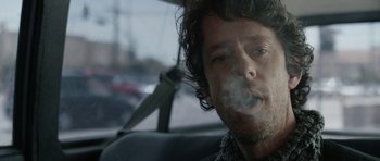 Movie still from “A Thousand Junkies” (2017), directed by Tommy Swerdlow – A man sitting in the back seat of a car smoking; Close Up shot, Low angle