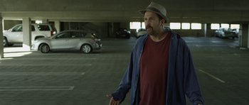 Movie still from “A Thousand Junkies” (2017), directed by Tommy Swerdlow – A man wearing a hat standing in a parking lot; Medium shot, Over the shoulder angle