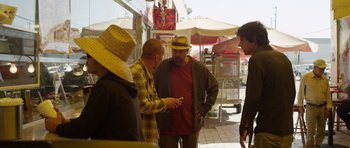 Movie still from “A Thousand Junkies” (2017), directed by Tommy Swerdlow – A group of men standing around looking at a cell phone; Medium shot, Over the shoulder angle