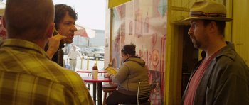 Movie still from “A Thousand Junkies” (2017), directed by Tommy Swerdlow – A woman sitting at an outdoor table eating a meal; Medium shot, Over the shoulder angle