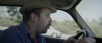 Movie still from “A Thousand Junkies” (2017), directed by Tommy Swerdlow – A man with a hat is looking out of a car window; Close Up shot, Over the shoulder angle