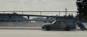 Movie still from “A Thousand Junkies” (2017), directed by Tommy Swerdlow – A car driving down a street next to an overpass; Extreme Wide shot, High angle