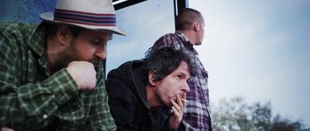 Movie still from “A Thousand Junkies” (2017), directed by Tommy Swerdlow – Three men sitting on a bench eating food; Medium shot, Low angle