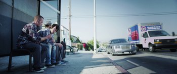 Movie still from “A Thousand Junkies” (2017), directed by Tommy Swerdlow – A man sitting on the side of the street looking at his phone; Wide shot, Low angle