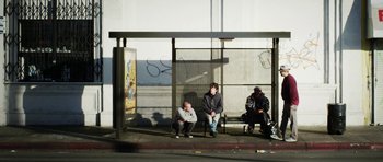Movie still from “A Thousand Junkies” (2017), directed by Tommy Swerdlow – A group of men sitting on a bench next to a sidewalk; Wide shot, High angle