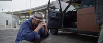 Movie still from “A Thousand Junkies” (2017), directed by Tommy Swerdlow – A man sitting on the side of the road next to an open car door; Close Up shot, Low angle