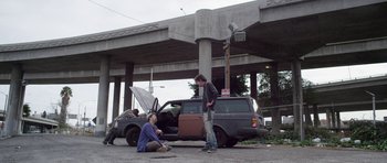 Movie still from “A Thousand Junkies” (2017), directed by Tommy Swerdlow – A man and a woman standing in front of a car; Wide shot, Low angle