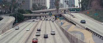 Movie still from “A Thousand Junkies” (2017), directed by Tommy Swerdlow – Cars are driving on a freeway near a bridge; Extreme Wide shot, High angle