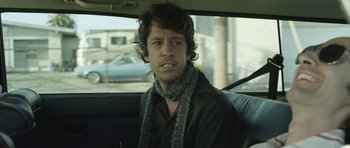 Movie still from “A Thousand Junkies” (2017), directed by Tommy Swerdlow – A man sitting in the back of a car wearing a scarf; Close Up shot, Over the shoulder angle