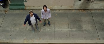 Movie still from “A Thousand Junkies” (2017), directed by Tommy Swerdlow – Two men standing on the steps of a building; Wide shot, Overhead angle