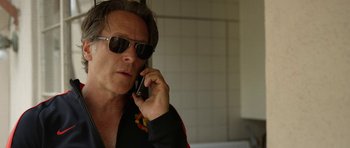 Movie still from “A Thousand Junkies” (2017), directed by Tommy Swerdlow – A man wearing sunglasses talking on a cell phone; Close Up shot, Over the shoulder angle