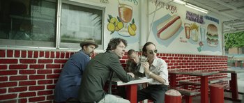 Movie still from “A Thousand Junkies” (2017), directed by Tommy Swerdlow – A group of men sitting at a table in a restaurant; Medium shot, Low angle