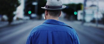 Movie still from “A Thousand Junkies” (2017), directed by Tommy Swerdlow – A man wearing a blue shirt and a gray hat; Close Up shot, Low angle