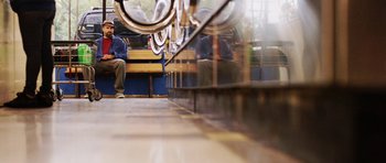 Movie still from “A Thousand Junkies” (2017), directed by Tommy Swerdlow – A man sitting on a bench next to a bicycle; Wide shot, Low angle