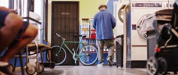 Movie still from “A Thousand Junkies” (2017), directed by Tommy Swerdlow – A man in a blue jacket and a green bicycle; Wide shot, Low angle