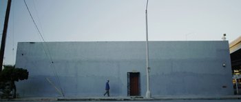 Movie still from “A Thousand Junkies” (2017), directed by Tommy Swerdlow – A man walking down the sidewalk near a building; Wide shot, Low angle