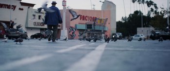 Movie still from “A Thousand Junkies” (2017), directed by Tommy Swerdlow – A man walking down a street with a shopping cart; Wide shot, Low angle