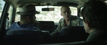Movie still from “A Thousand Junkies” (2017), directed by Tommy Swerdlow – Two men sitting in the back seat of a car; Medium shot, Over the shoulder angle