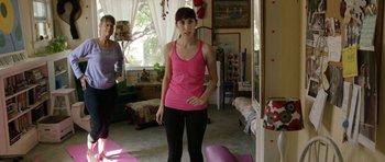 Movie still from “A Thousand Junkies” (2017), directed by Tommy Swerdlow – A woman in a pink shirt standing in a room; Medium shot, Over the shoulder angle