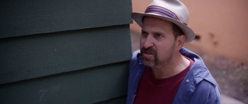 Movie still from “A Thousand Junkies” (2017), directed by Tommy Swerdlow – A man wearing a hat leaning against a wall; Close Up shot, Over the shoulder angle