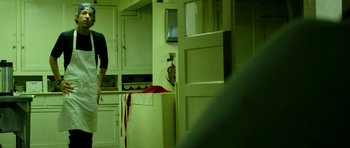 Movie still from “A Thousand Junkies” (2017), directed by Tommy Swerdlow – A person standing in a kitchen with a knife on the counter; Medium shot, Over the shoulder angle