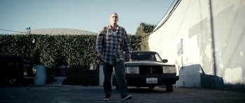 Movie still from “A Thousand Junkies” (2017), directed by Tommy Swerdlow – A man walking in front of a car in a parking lot; Wide shot, Low angle