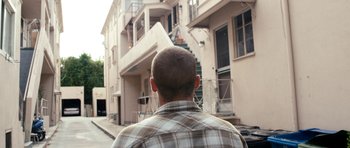 Movie still from “A Thousand Junkies” (2017), directed by Tommy Swerdlow – A man in a plaid shirt is looking at a building; Wide shot, Low angle