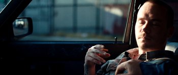 Movie still from “A Thousand Junkies” (2017), directed by Tommy Swerdlow – A person sitting in a car smoking a cigarette; Close Up shot, Over the shoulder angle