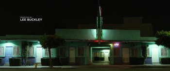 Movie still from “A Thousand Junkies” (2017), directed by Tommy Swerdlow – A building that is lit up at night time; Extreme Wide shot, Low angle