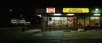 Movie still from “A Thousand Junkies” (2017), directed by Tommy Swerdlow – A fast - food restaurant at night with the lights on; Extreme Wide shot, Low angle