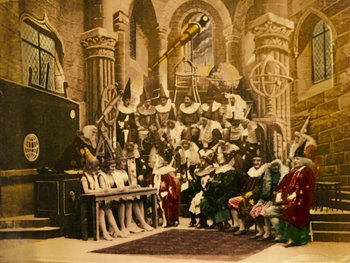 Movie still from “A Trip to the Moon” (1902), directed by Georges Méliès – A group of people sitting in a room with a large painting; Extreme Wide shot, Low angle