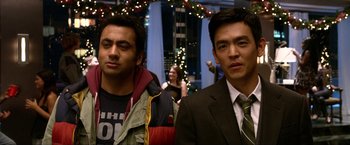 Movie still from “A Very Harold & Kumar Christmas” (2011), directed by Todd Strauss-Schulson – A couple of men standing next to each other in front of lights; Close Up shot, Over the shoulder angle