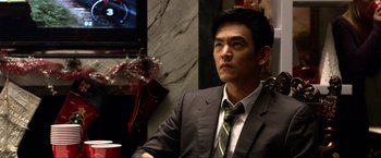 Movie still from “A Very Harold & Kumar Christmas” (2011), directed by Todd Strauss-Schulson – A man wearing a suit and tie sitting at a table in front of a television; Close Up shot, Over the shoulder angle
