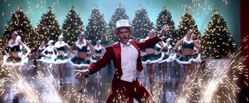 Movie still from “A Very Harold & Kumar Christmas” (2011), directed by Todd Strauss-Schulson – A man in a red suit and white hat is in front of a group of dancers; Wide shot, Low angle