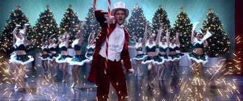 Movie still from “A Very Harold & Kumar Christmas” (2011), directed by Todd Strauss-Schulson – A man in a red suit and a white hat holding a red cane in front of a group of people; Extreme Wide shot, Low angle